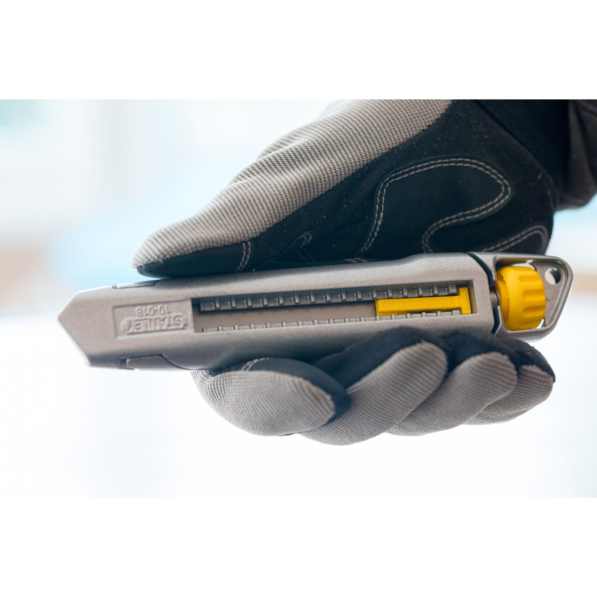 Photo of STANLEY 0-10-018 utility knife with gray and yellow design, held in a gloved hand, side view.