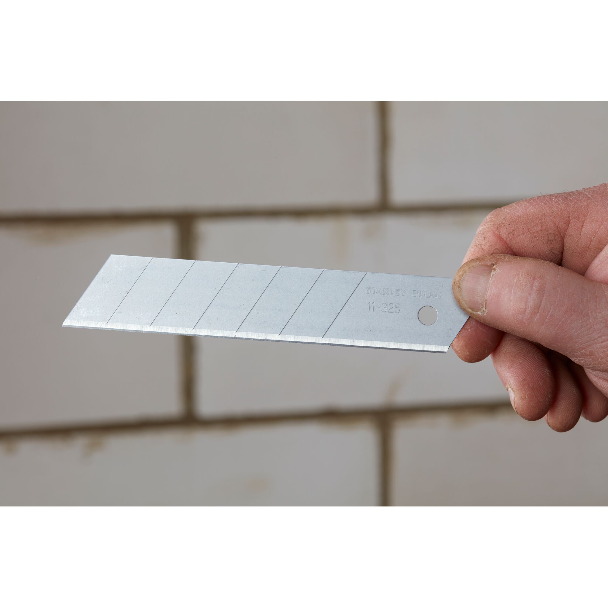 Photo of STANLEY 0-11-325 snap-off utility knife blade held by hand, silver color, multiple snap lines visible.