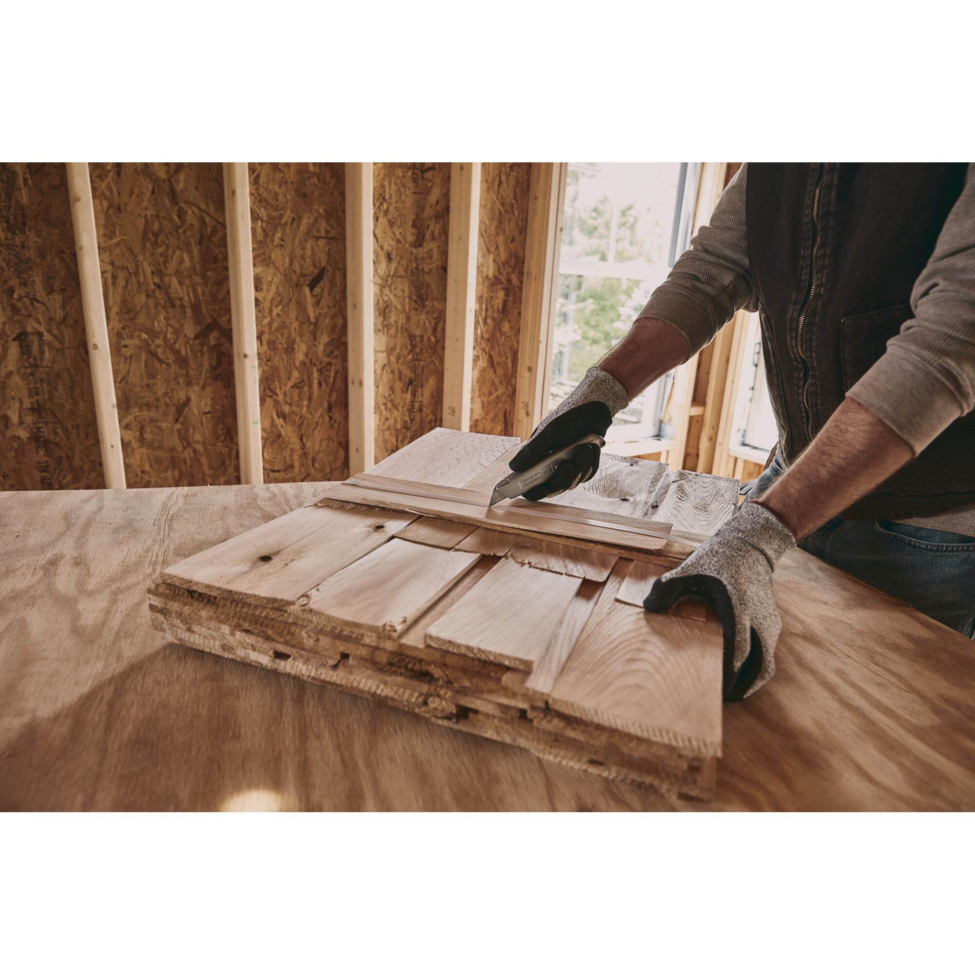 Photo of STANLEY 10-099 utility knife cutting wood in a workshop, close-up of hands wearing gloves.