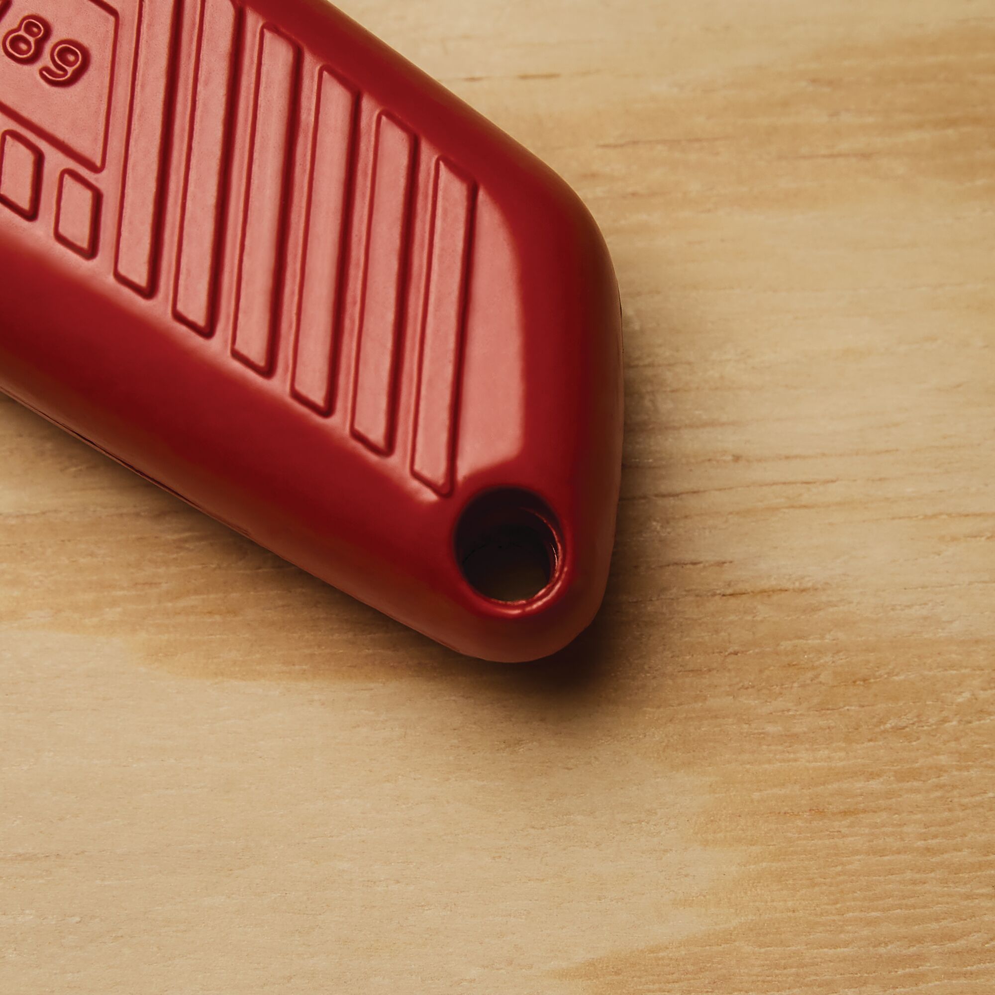 Stanley 10-189C red utility knife handle with textured grip, close-up on wood surface.