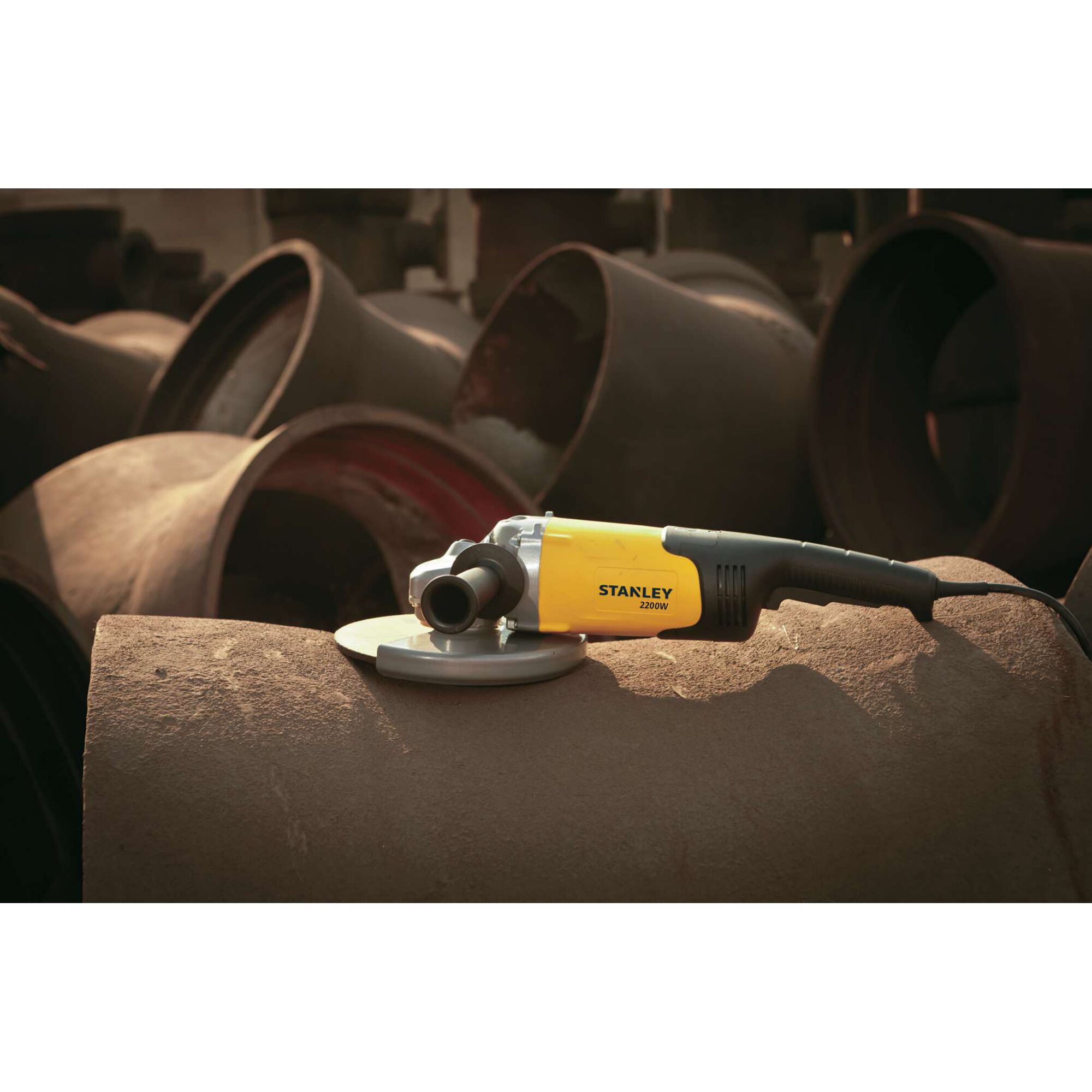 Photo of STANLEY SL229-B3 angle grinder with yellow and black body resting on a large metal pipe in an industrial setting.