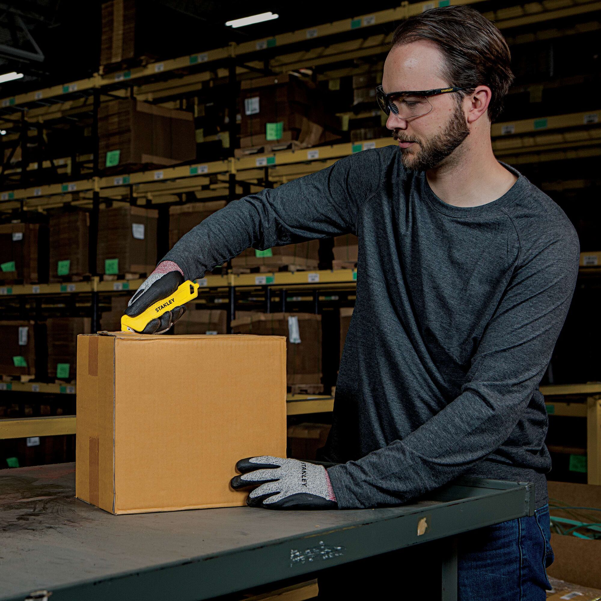 Stanley STHT10355 utility knife used to open a cardboard box on a warehouse table.