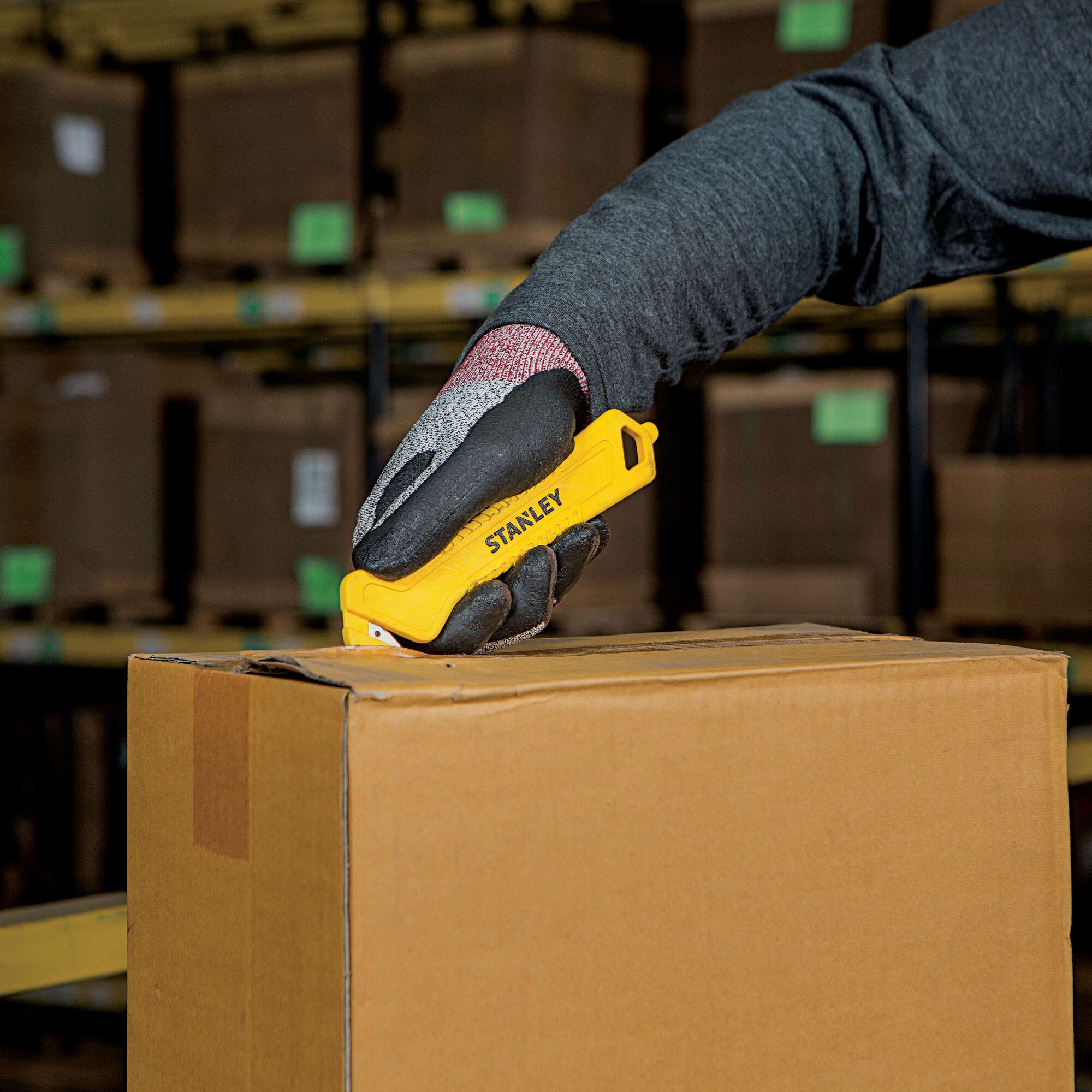 Stanley STHT10355 yellow utility knife used to cut open a cardboard box in a warehouse.