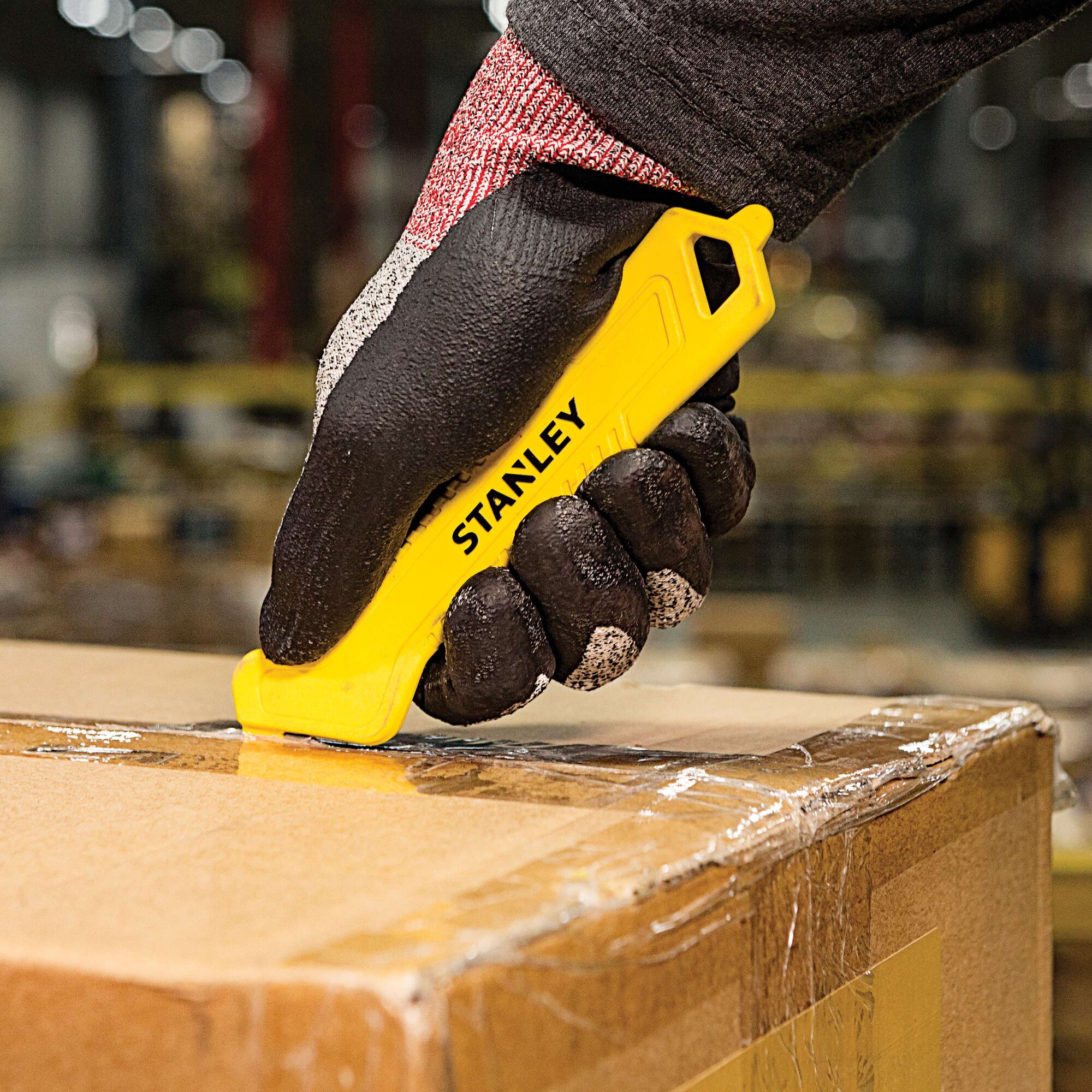 STANLEY STHT10355 yellow safety knife in gloved hand cutting box tape, close-up photography.