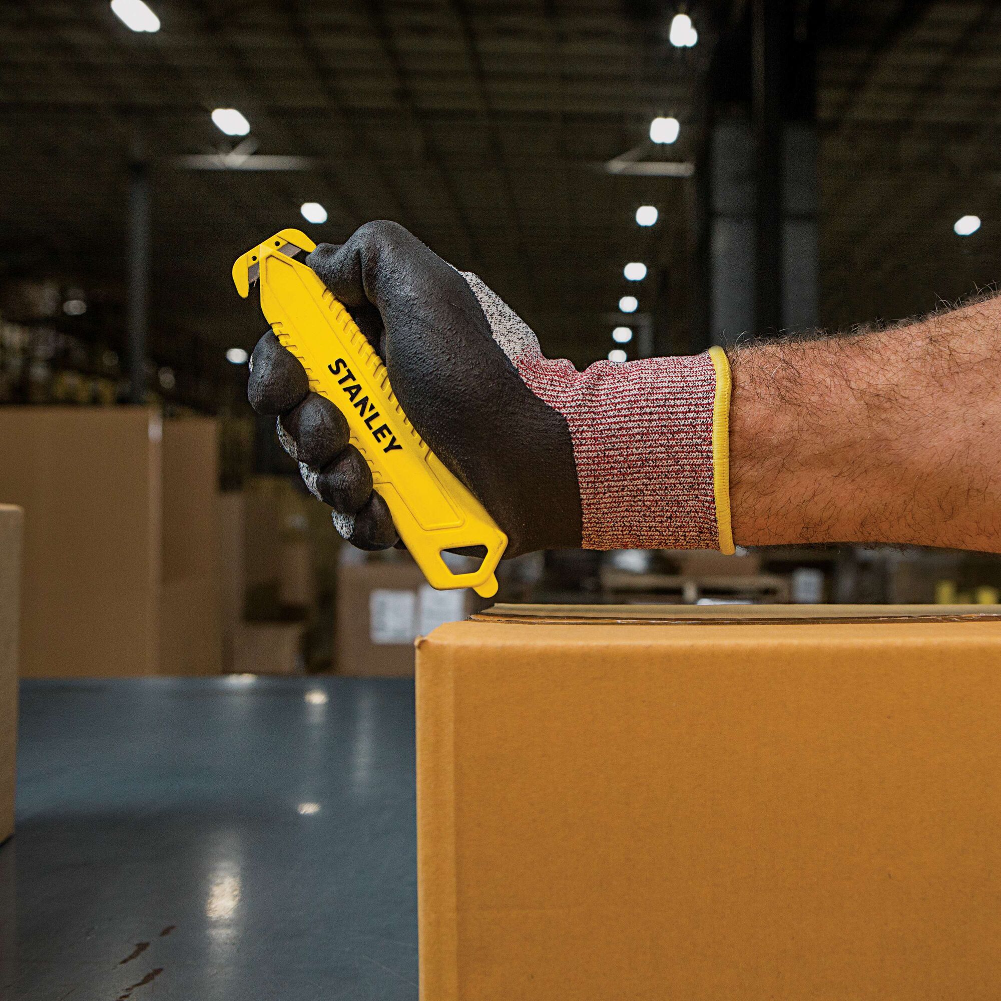 Stanley STHT10359 safety knife used to cut a cardboard box, shown in a warehouse setting.