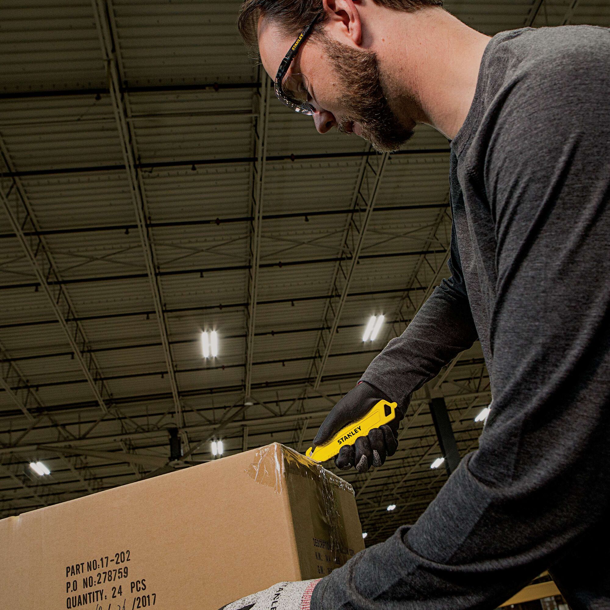 Stanley STHT10359 yellow utility knife used to open a cardboard box in an industrial warehouse setting.